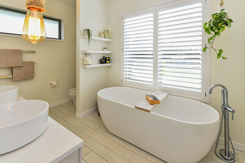 Large freestanding bath under large picture window with shutters and view. Double round basins with rope pendents