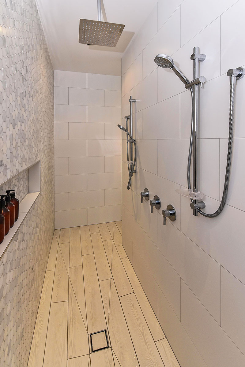 Large walk through double shower with marble mosaic feature wall, wooden floor tiles and rainhead