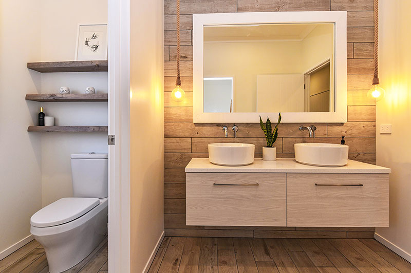 Wooden floor & wall tiles, light wood double vanity with round basins, hanging rope pendent lights & rustic shelves in toilet