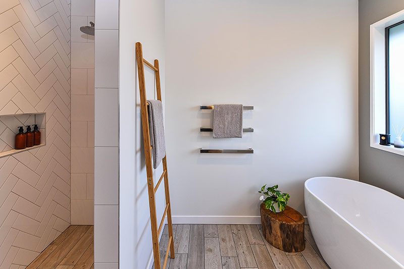 Shower with herringbone tile feature wall and wood floor tiles with freestanding bath, wooden ladder and stump decor 