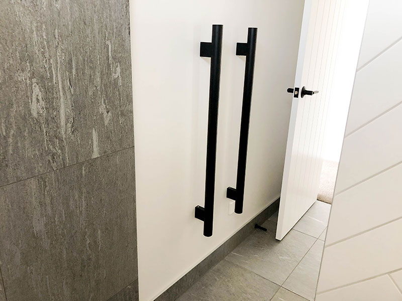 Black vertical heated towel rails with grey tiled wall and floor and white subway herringbone