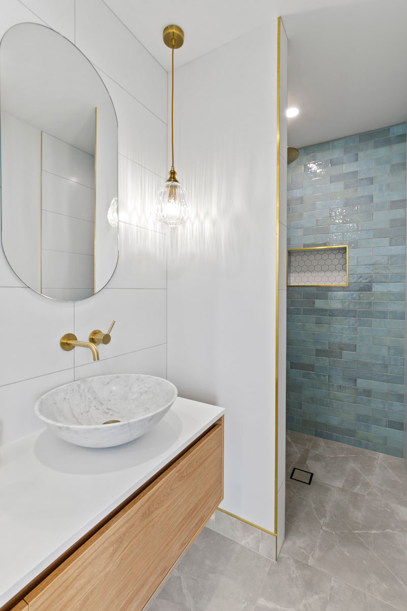 Gorgeous light bathroom with blue subway tiles in shower from Tile Space and brass trim. Feature light