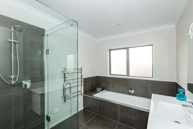 Simple bathroom design with grey brown tiles, in shower and around bath with glass shower frame