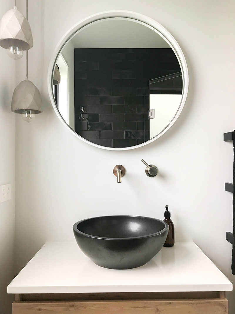 Timber vanity with charcoal basin, white round mirror, concrete pendent lights and charcoal subway tiles in shower 