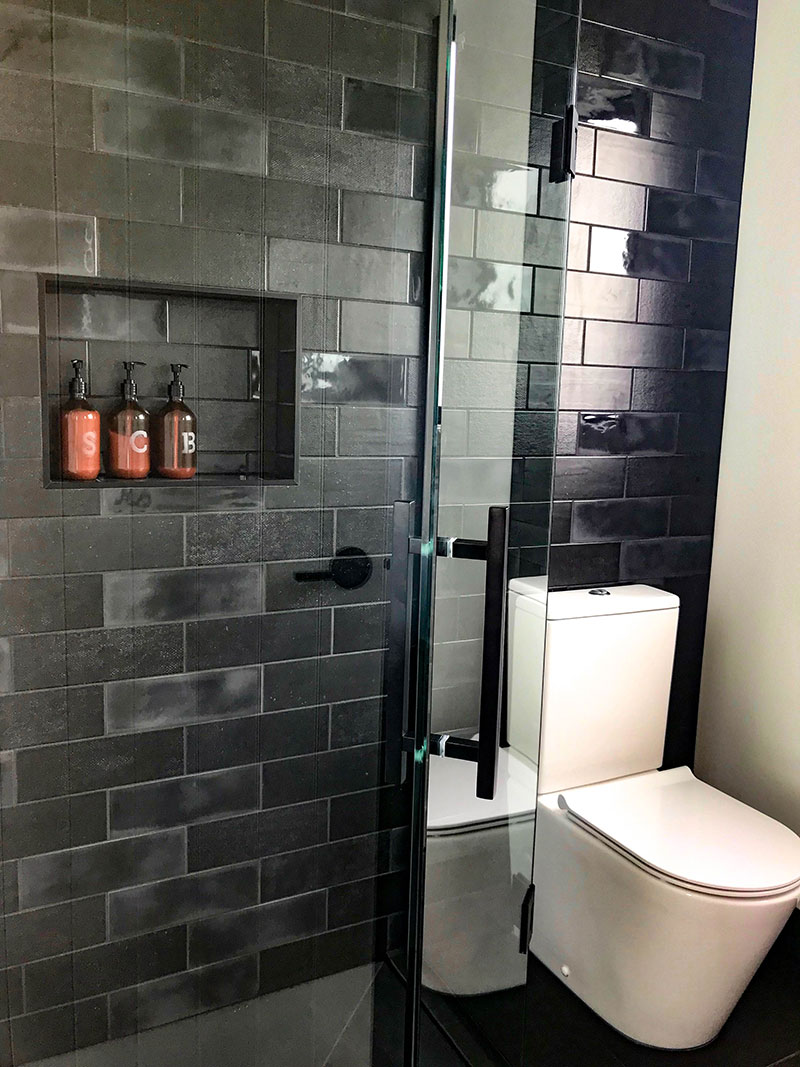Charcoal / black diesel subway tiles on ensuite feature wall with recess shelf and glass shower frame with black details