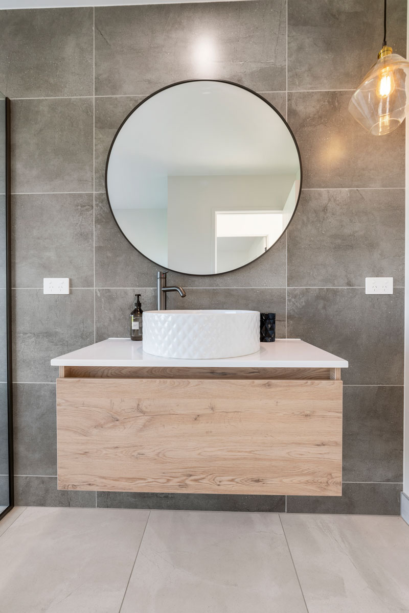 Gorgeous grey tiled wall in bathroom with large round mirror, timber New Tech vanity, Robertson basin