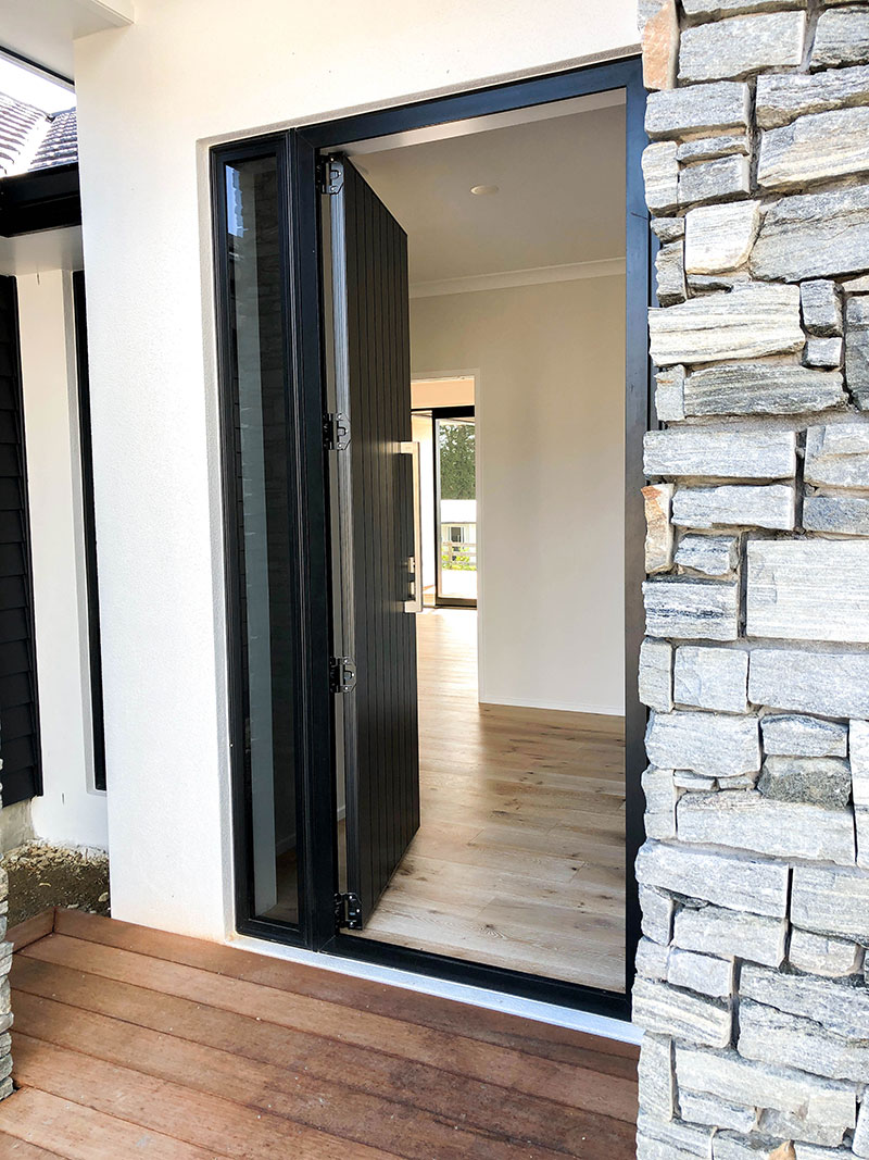 Entrance to new home with schist pillars, wooden deck, black front door and white plaster