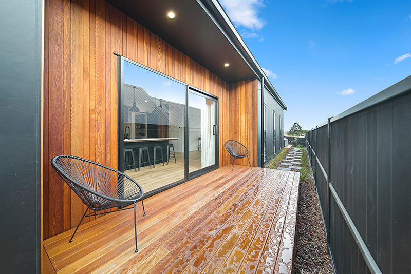 Exterior kitchen deck with black chairs with cedar clad wall and black fence