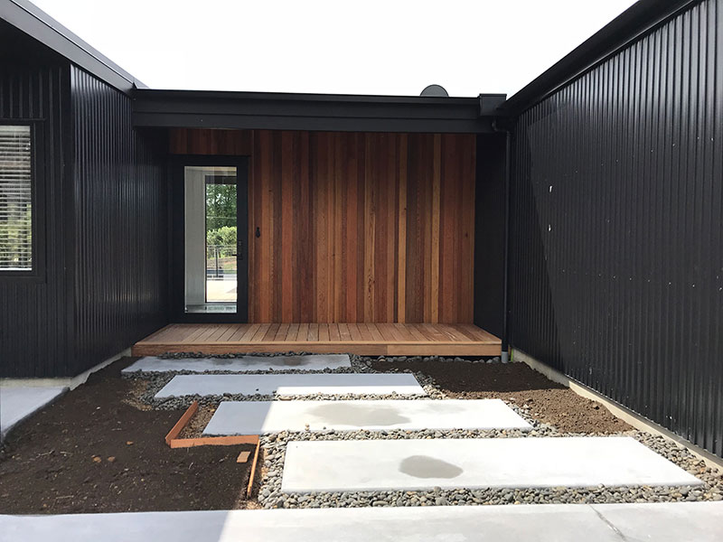 entrance to black barn style house with cedar feature and concrete slab path with stones