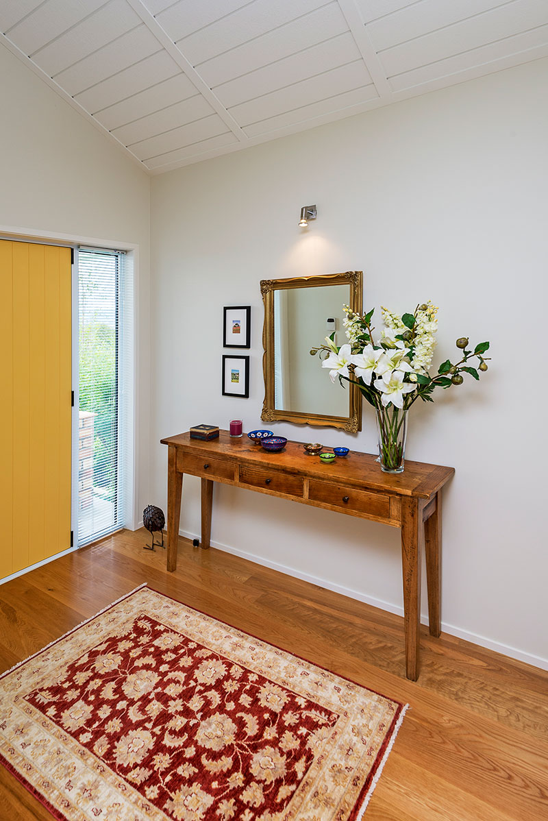 yellow front door in entry with raking, panelled ceilings and timber floor with rug