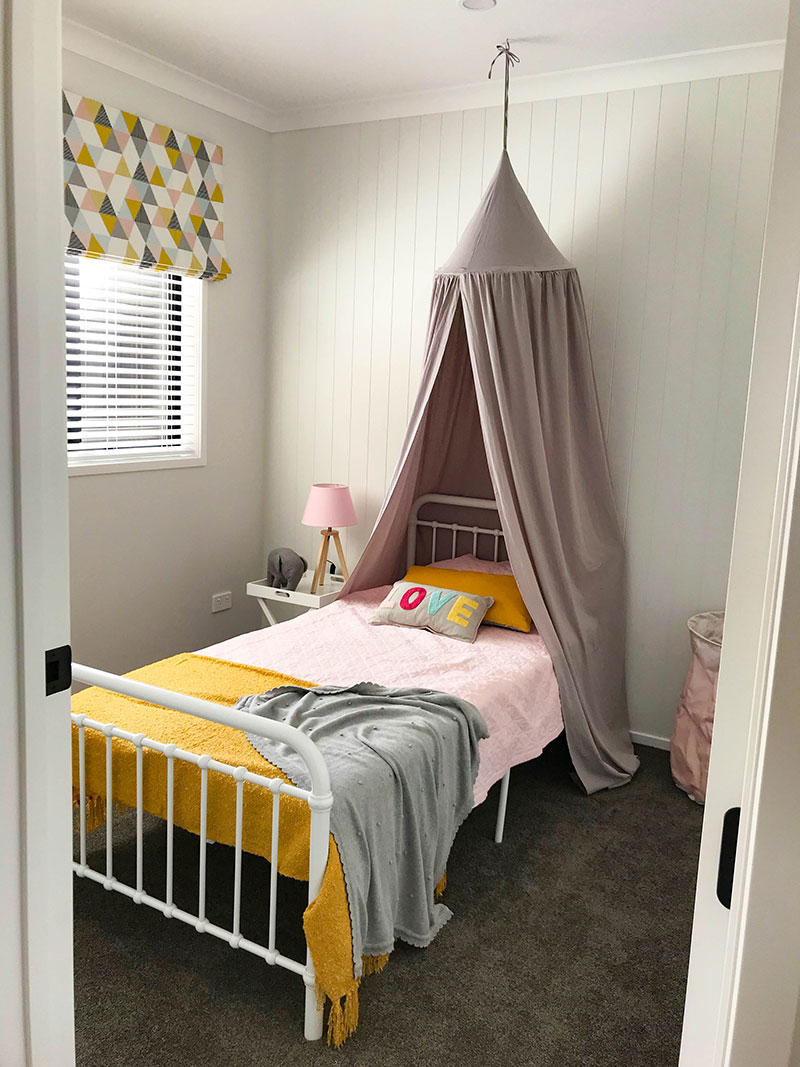 childrens bedroom with grey bed canopy pink, grey and yellow mustard geometric roman blind