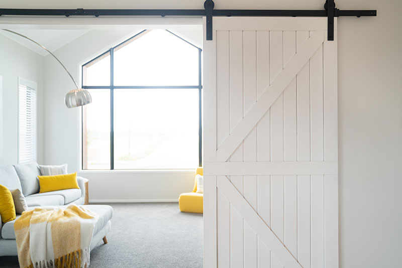 white rustic barn door with black runners on entrance to yellow and grey lounge