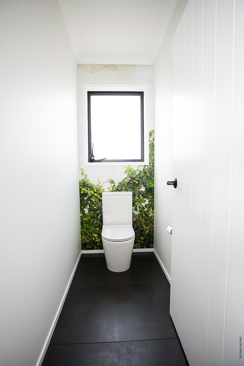 Toilet with dark charcoal tiles and mural wallpaper of ivy on concrete wall