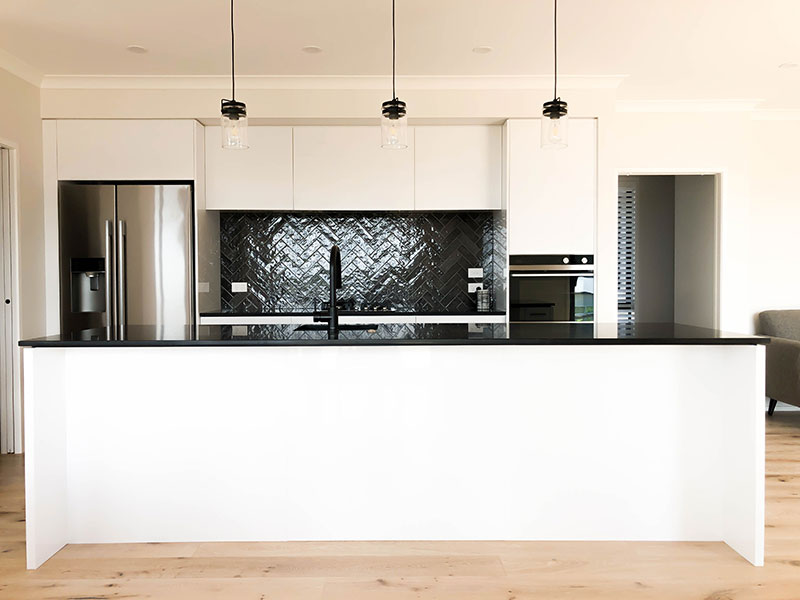 Black and white kitchen with island bench, herringbone charcoal splashback and hanging pendent lights