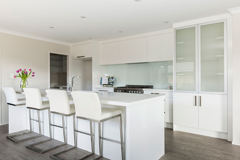 Simple White kitchen with island bench, cut glass coloured splashback and timber floor