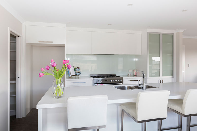 Beautiful light white kitchen with island bench. white barstools and vase of pink tulips