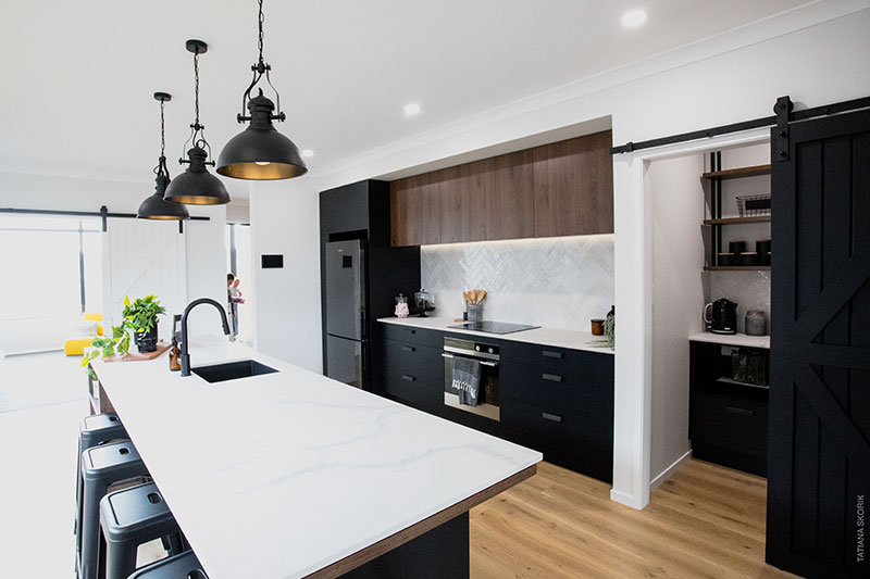 White bench top and black cabinets in showhome kitchen at Paerata Rise. Black barn door & scullery with suspended shelves