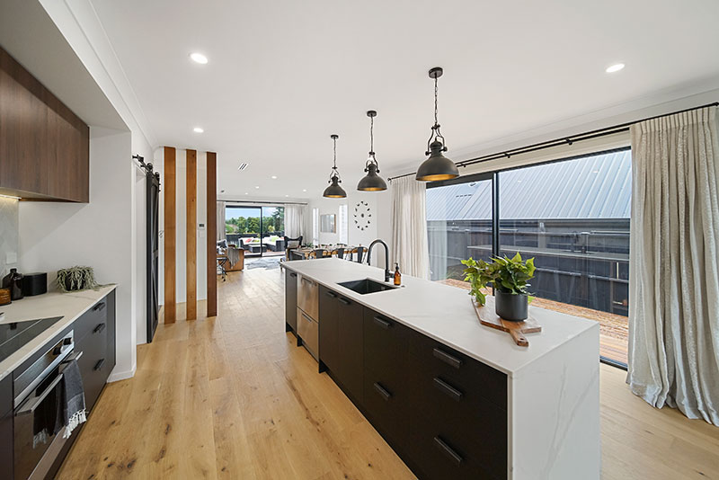 Black kitchen cabintery with white marble benchtop, cedar posts, timber floor and black pendent lights