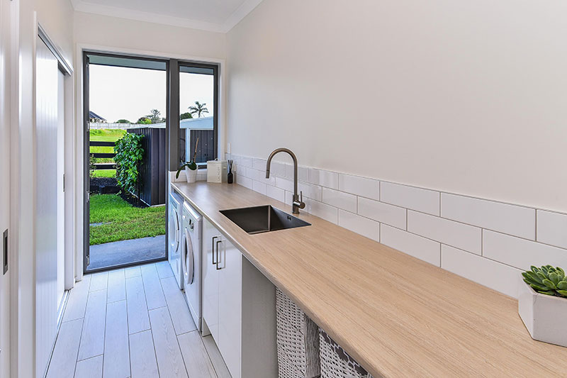 Expansive timber look bench in Laundry with subway tiles splashback, white cabinets and large sink