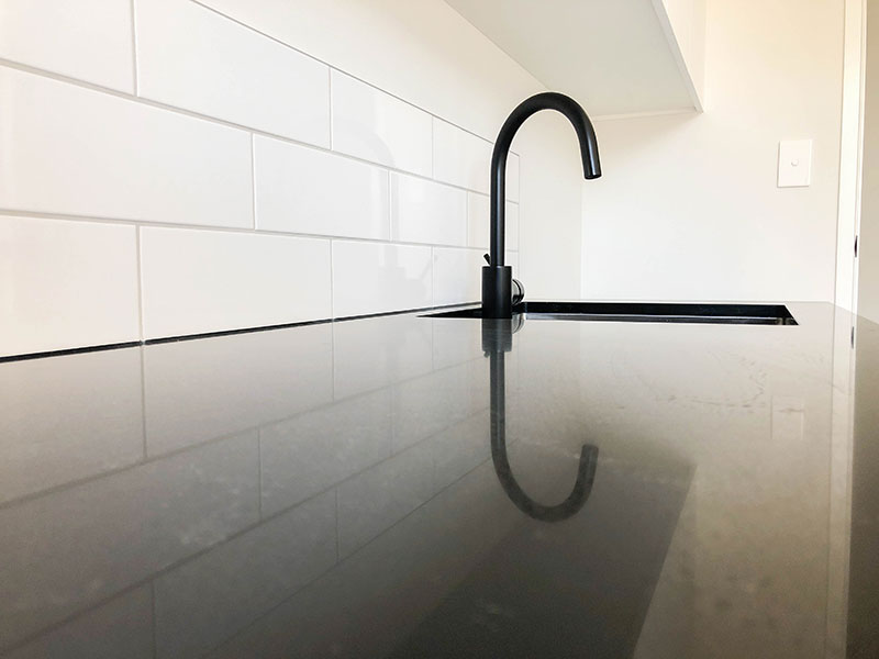 Black marble benchtop in laundry with white subway tiled splashback, brushed stainless sink and black tap