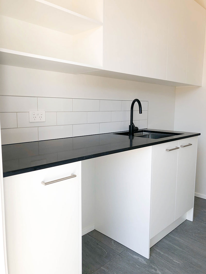Black and white laundry with black benchtop and white cabinets, grey tiled floor and white subway