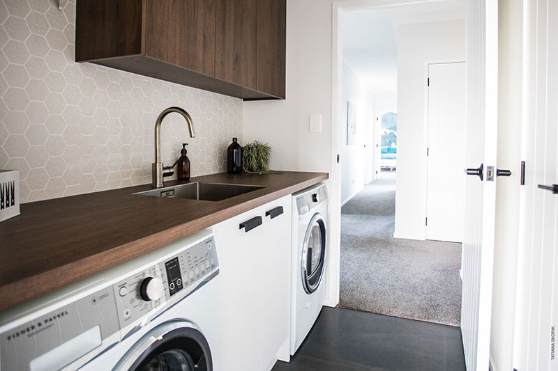 Stunning laundry with timber look bench and cabinets, stitch Mosaic tile splashback and dark tiled floor
