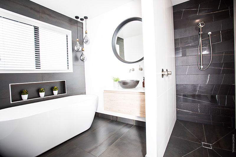 Luxurious Bathroom with charcoal floor tiles and feature wall behind bath. Black marble feature wall in shower