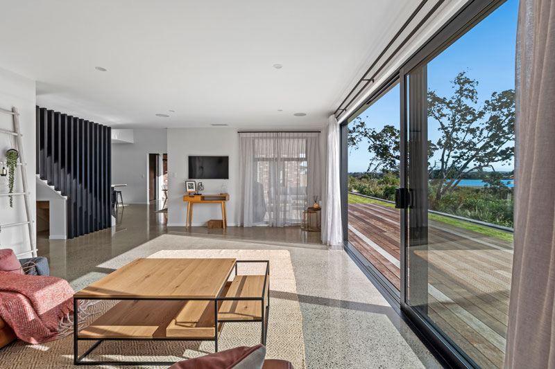 open sun drenched living space with concrete floors, timber linear staircase balustrade 
