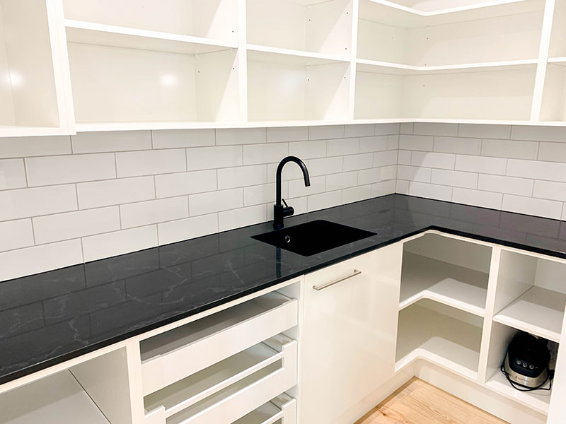Scullery with black marble benchtop, white cabinets, sink and white brick subway splashback