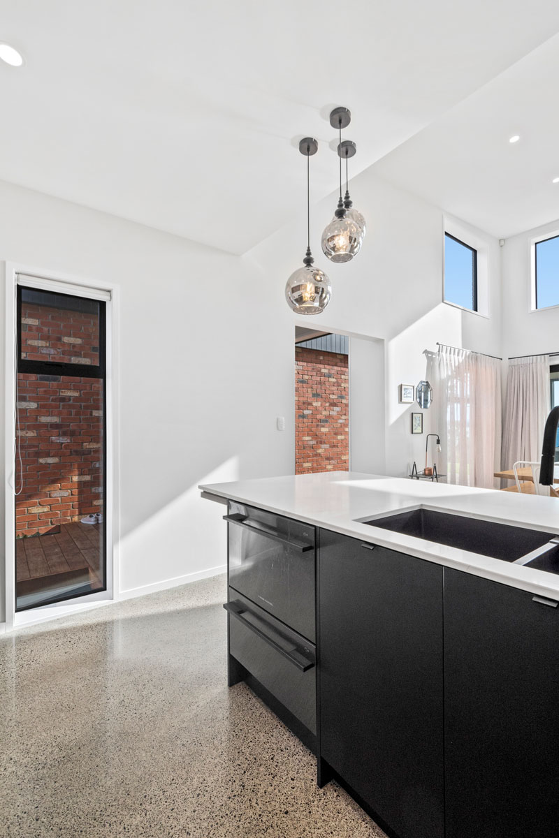 Gorgeous kitchen with black cabintry marble benchtop, and red brick feature wall in designer home in Glenbrook