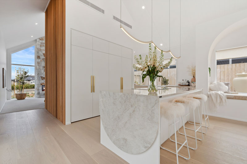 Gorgeous light mediterranean inspired kitchen with brass fittings, arched window seat, arch details on cabinets and benctop in Precision Homes showhome