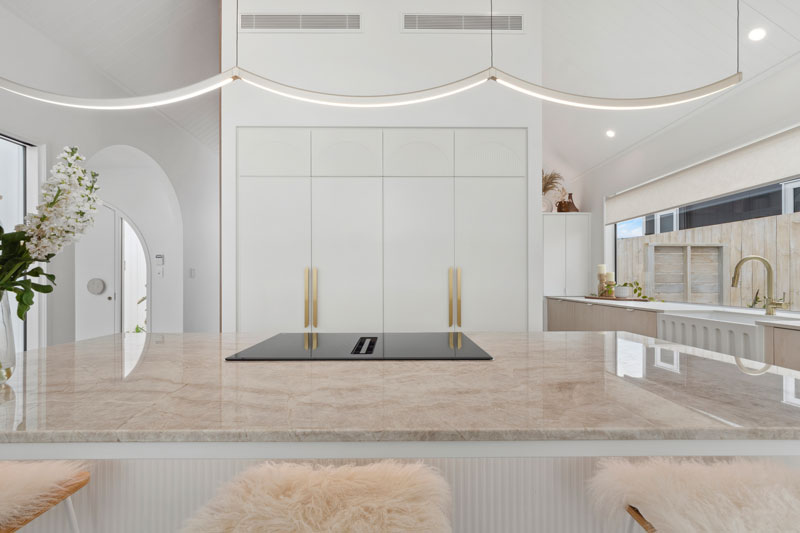 Gorgeous light mediterranean inspired kitchen with brass fittings, arched window seat, arch details on cabinets and benctop in Precision Homes showhome